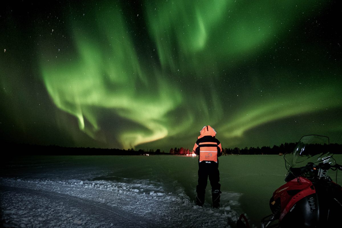 Snowmobile rider watching the Northern Lights in Levi