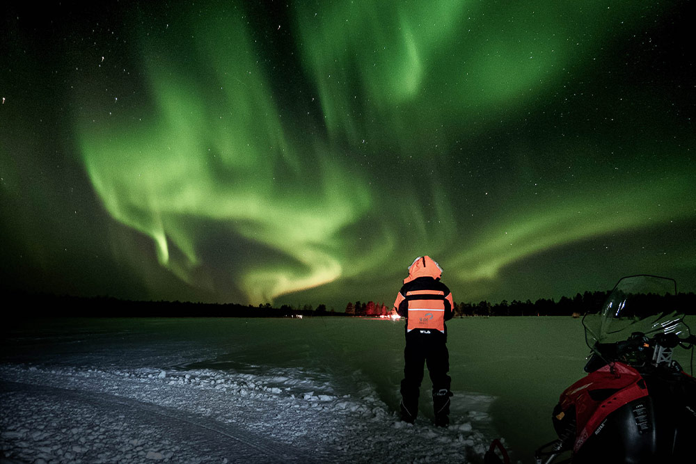 Snowmobiles parked beneath the Northern Lights in Levi