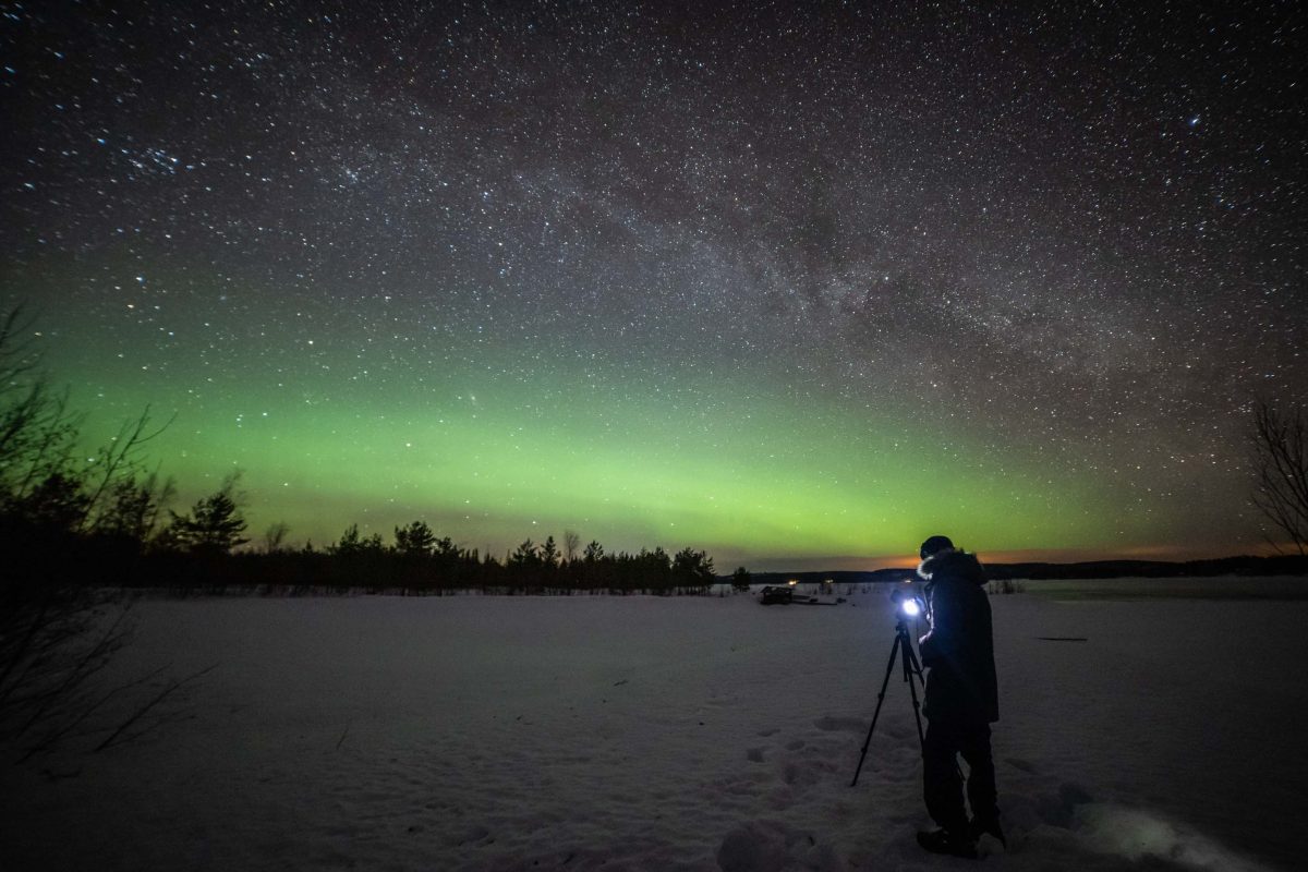 Photographer beneath the Aurora on a frozen lake