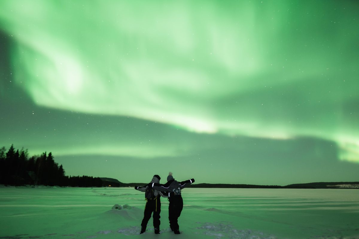 Couple watching the Northern Lights by an icy lake
