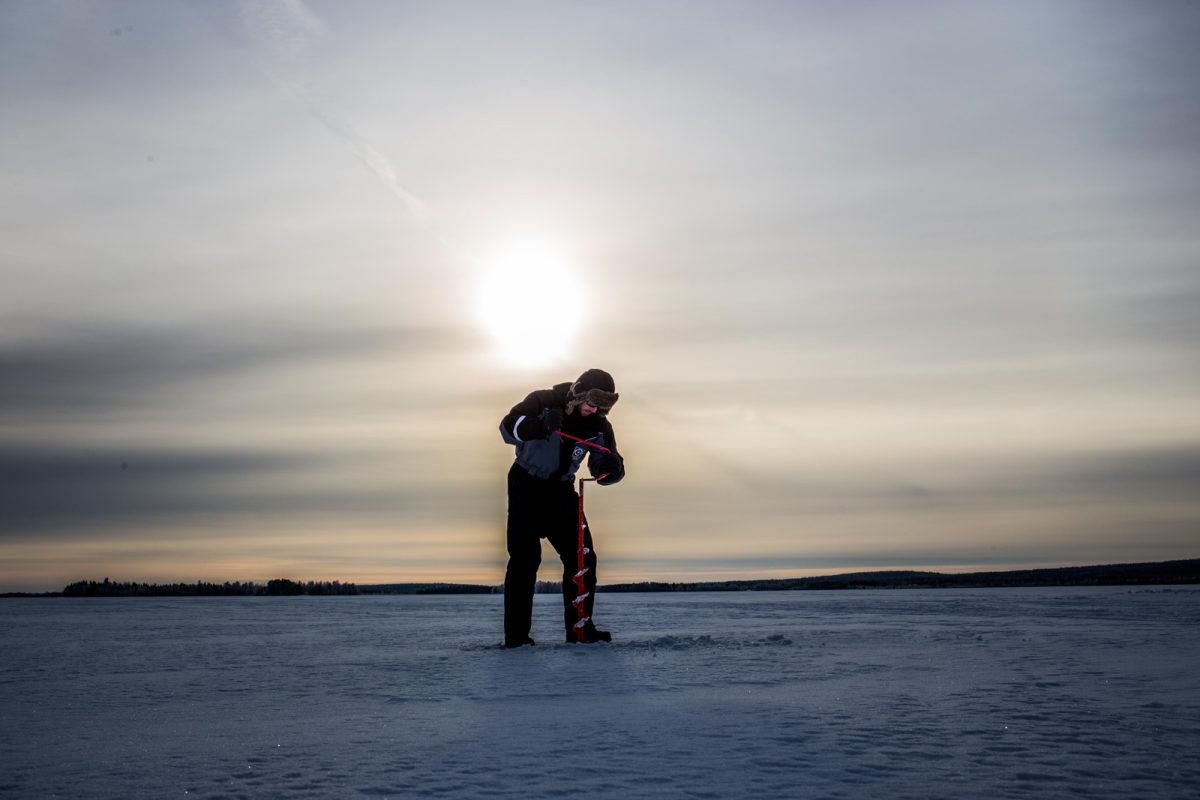 Drilling an ice-fishing hole on a frozen lake near Levi