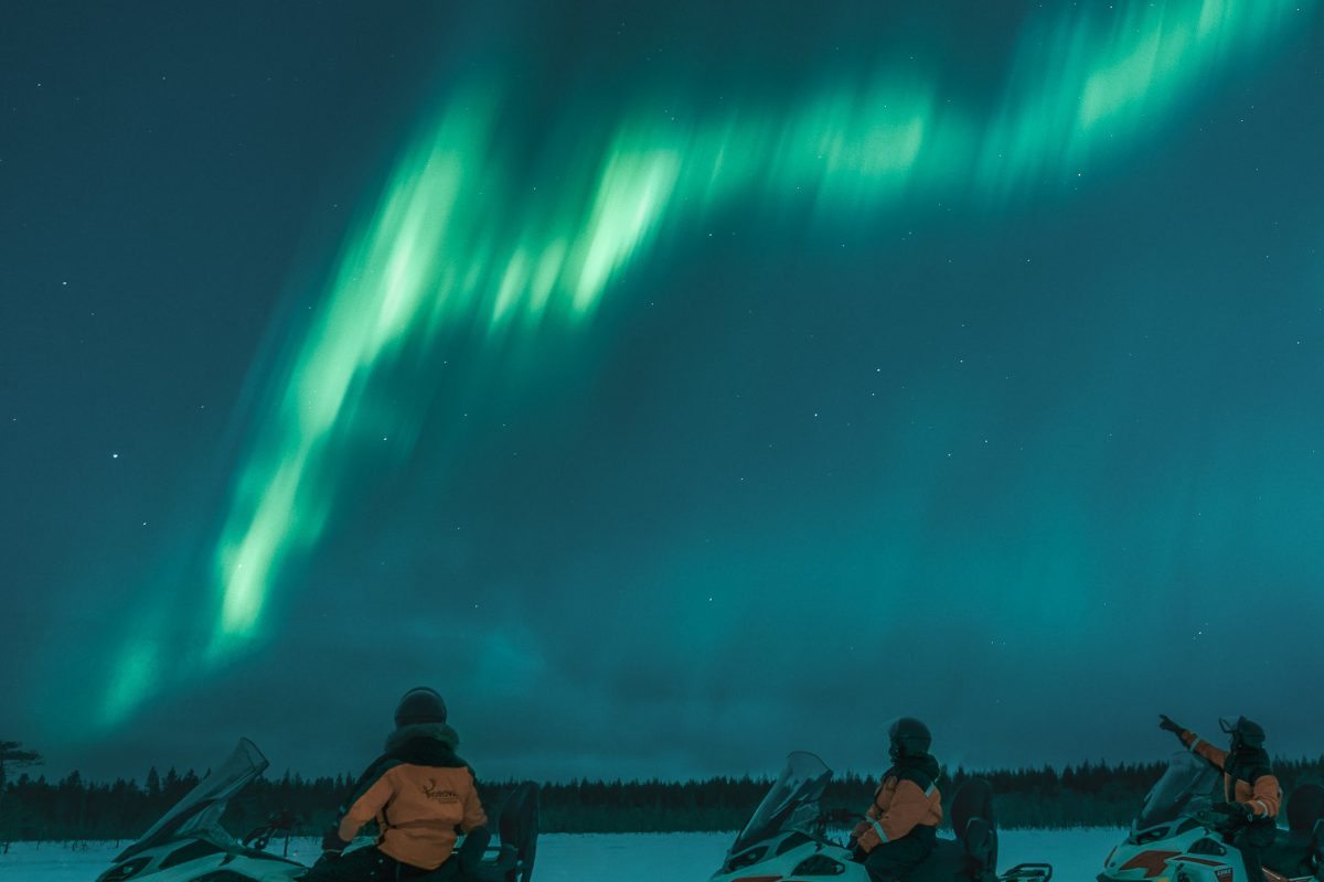Electric snowmobile riders stopping under the night sky in Rovaniemi