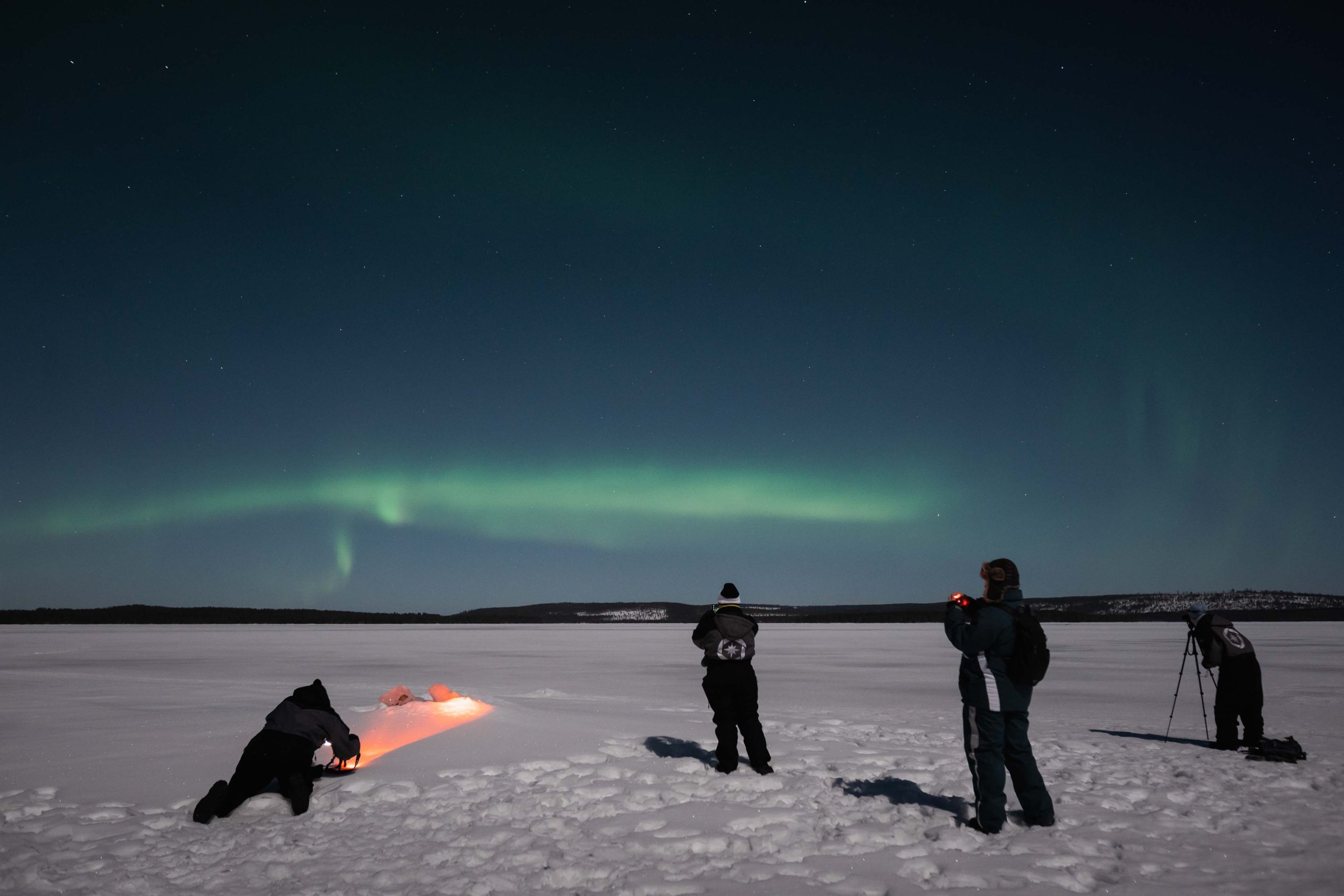 Small group photographing the northern lights on a frozen lake near Rovaniemi