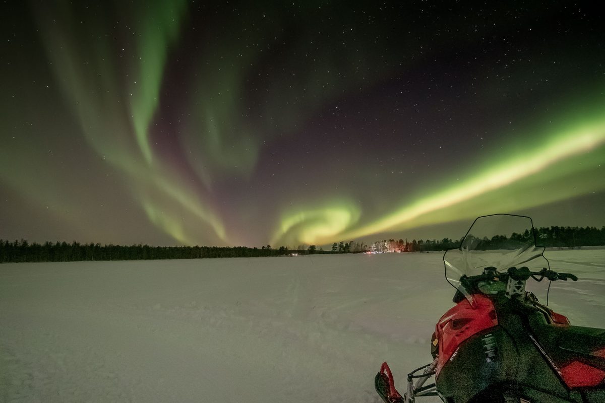 Riding a snowmobile towards the Northern Lights near Levi